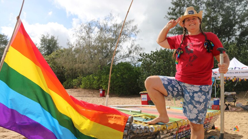 Beer Can Regatta competitor standing beside a single outrigger canoe adorned with a rainbow flag.
