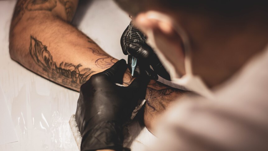someone using a tattoo gun with black gloved hands on a forearm