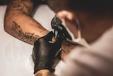 someone using a tattoo gun with black gloved hands on a forearm