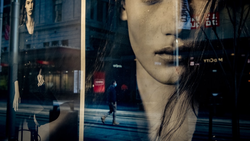 a shop window reflecting a man in a mask walking on an empty street