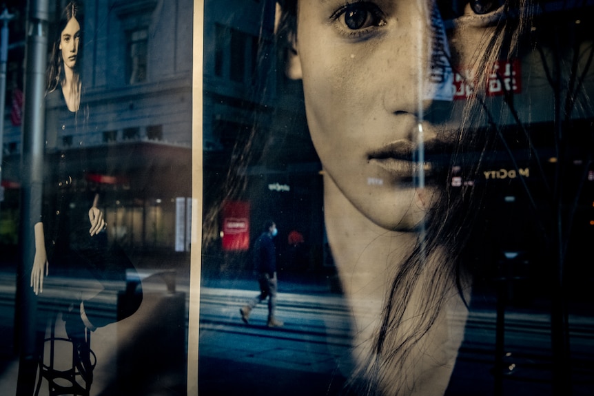 a shop window reflecting a man in a mask walking on an empty street