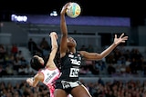 A Magpies netballer reaches out above her head to catch the ball ahead of a Thunderbirds defender. 
