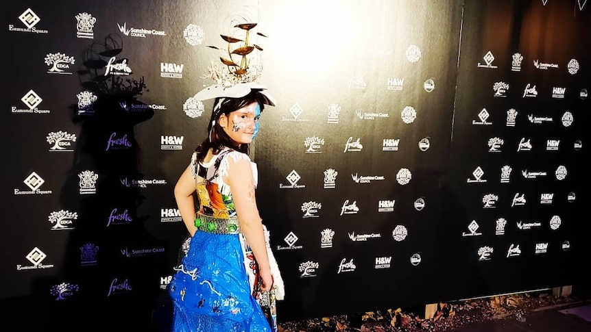 A young girl wears a brightly coloured dress on a fashion runway at night.