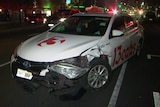 A damaged taxi at night with a police car behind