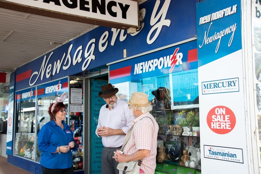 Man standing outside a newsagency talking to a woman and a man