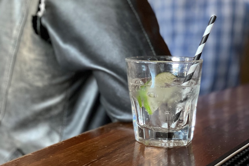 A mixed drink on a wooden table in the foreground with a man and woman out of focus on the background.