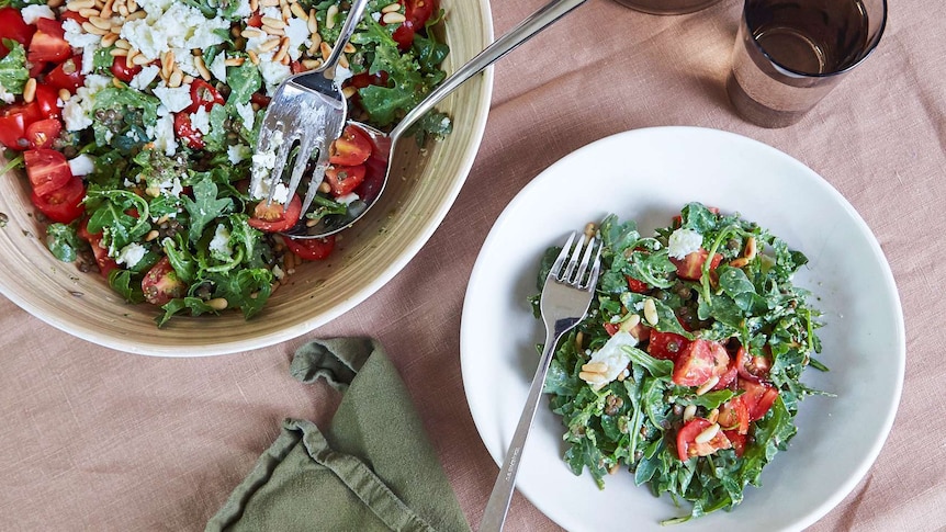 Lentil, rocket and pesto salad with feta cheese and cherry tomatoes in two bowls on a table setting.
