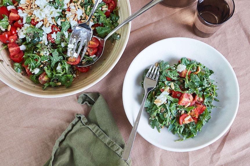 Lentil, rocket and pesto salad with feta cheese and cherry tomatoes in two bowls on a table setting.