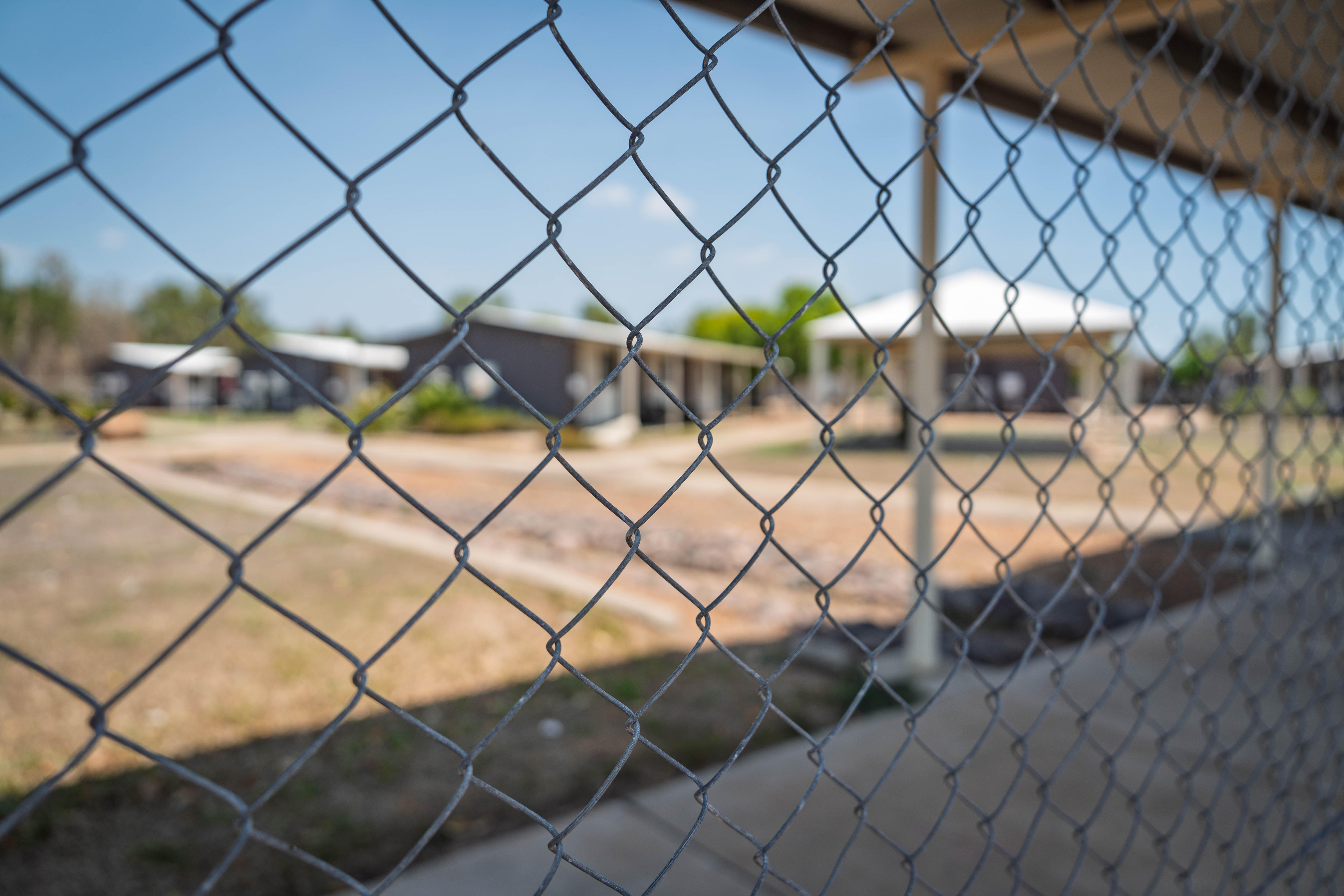 A short-stay accommodation facility, made up of small single-storey dwellings, viewed through a chain fence.