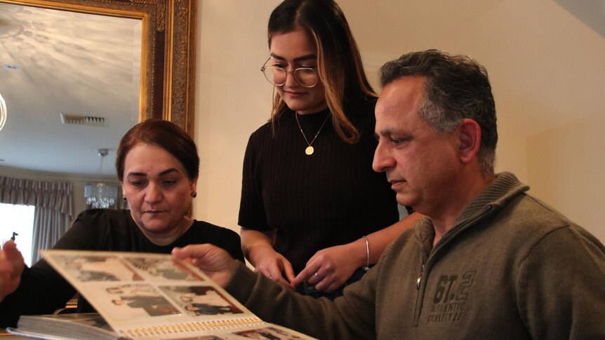 A young woman and her mother to her left and father to her right are looking at a photo album.