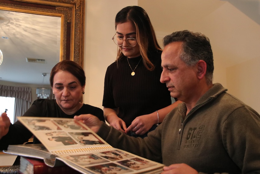 A young woman and her mother to her left and father to her right are looking at a photo album.