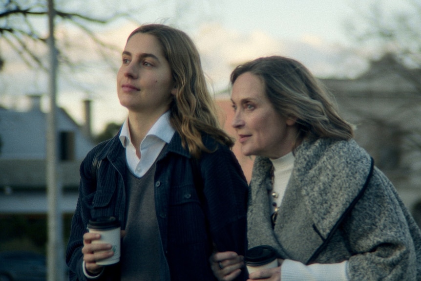 A 25-year-old woman with brown shoulder-length hair walks arm in arm with a woman in her 60s with grey hair