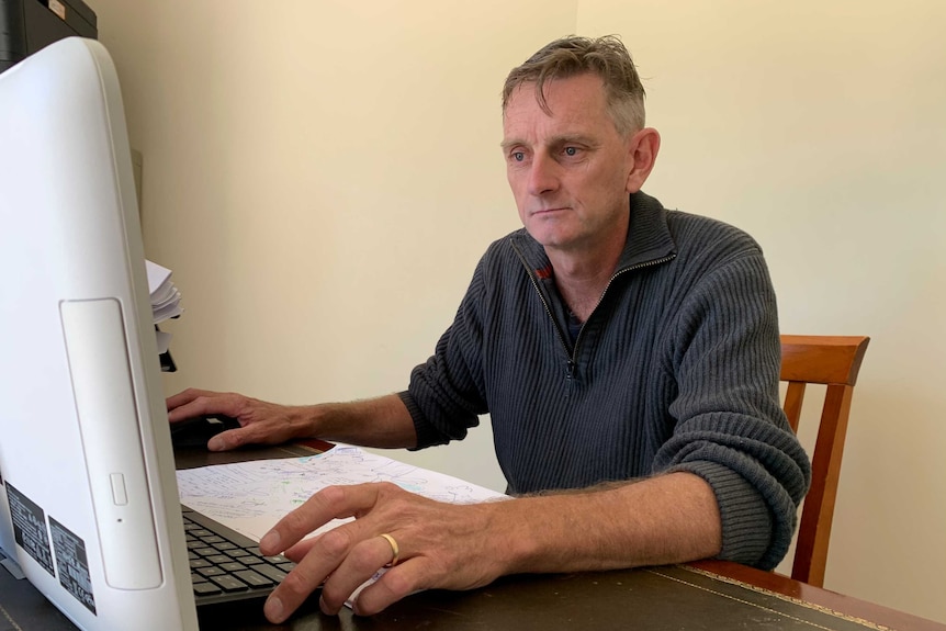 Simon sits at his computer with one hand on the mouse.