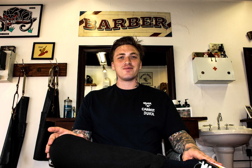 Jimmy Morrison sits crossed legged on barber shop chair, smiling at camera