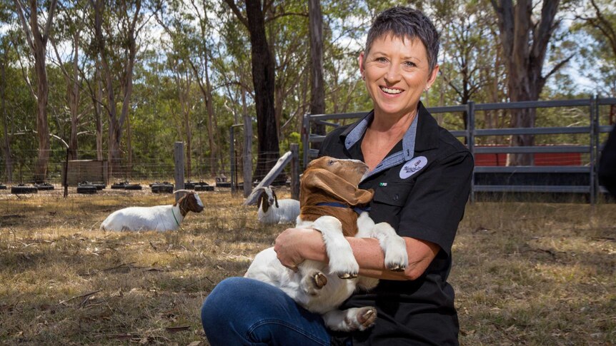 Violet Allan crouches holding a baby goat.