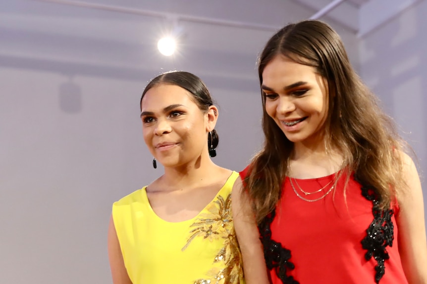 two Indigenous young girls wearing a red and and yellow matching outfits.