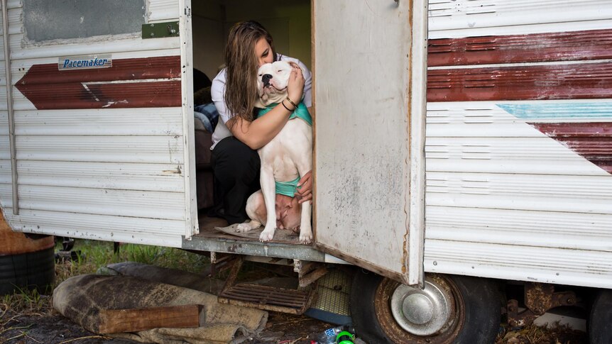 Breanna kisses her dog Lola in the doorway of her caravan.