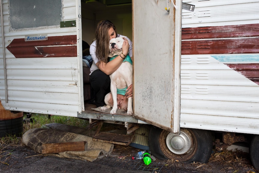 Breanna kisses her dog Lola in the doorway of her caravan.