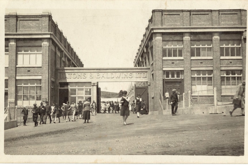 An historical black and white image of staff leaving and entering the Coats Patons building