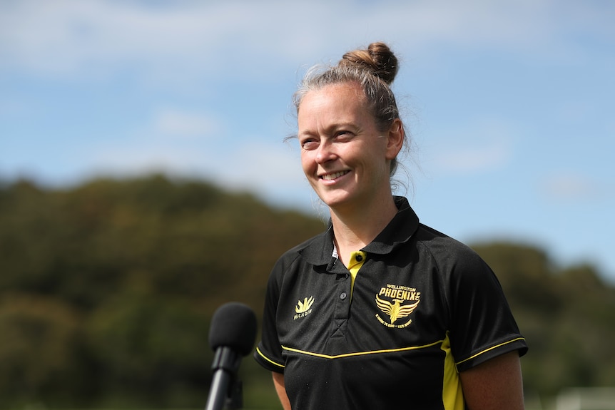 A woman wearing a black and yellow shirt with a phoenix crest smiles