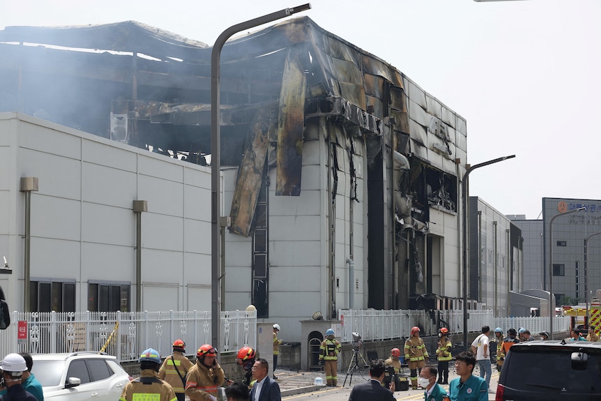 A charred building with firefighters in yellow uniform outside.