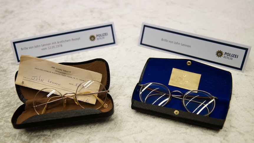 Two pairs of reading glasses sit on a table in their cases.