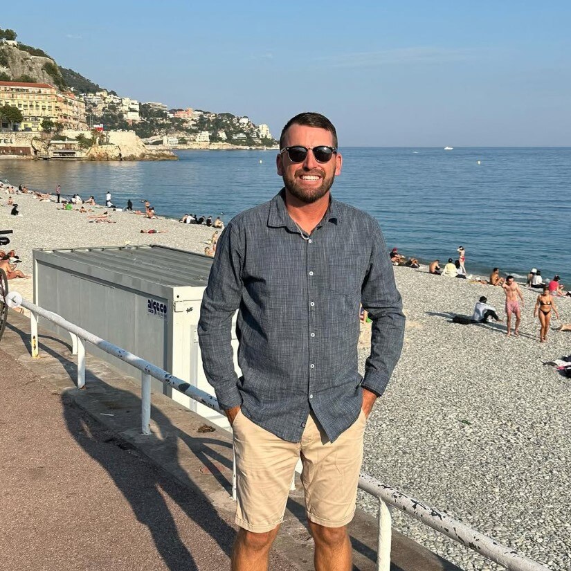 A man stands on a pebble beach.