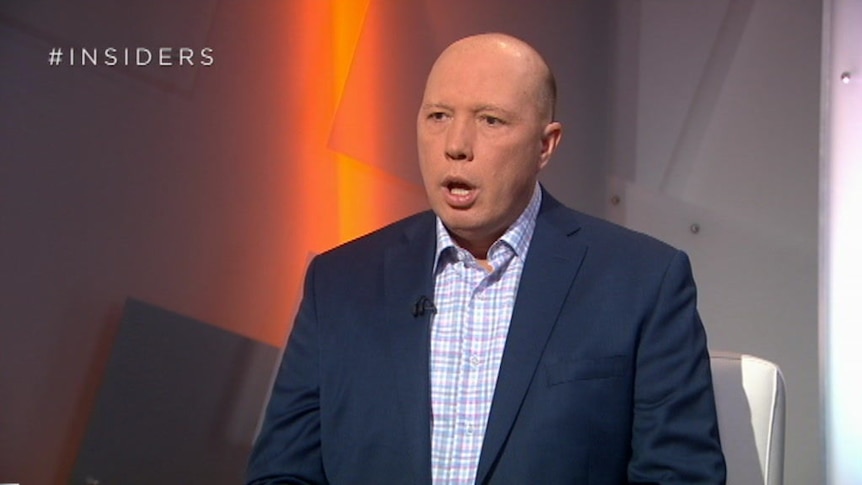 Peter Dutton wears a navy jacket and speaks while sitting on a white chair.