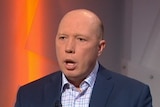 Peter Dutton wears a navy jacket and speaks while sitting on a white chair.