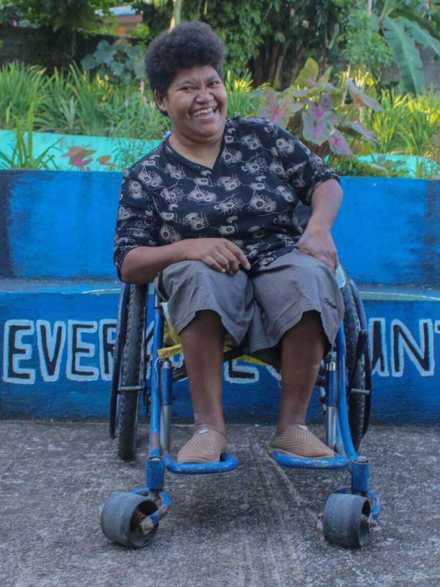 Femme en fauteuil roulant sourit à la caméra.
