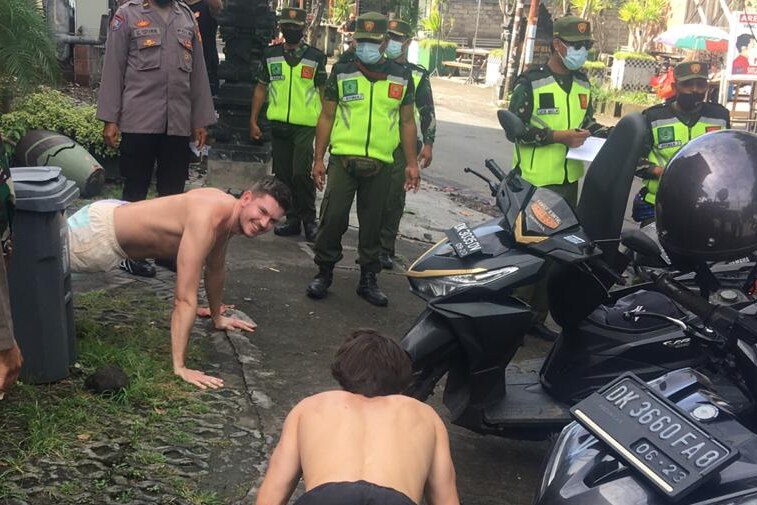 Two men doing push-ups on the streets of Bali surrounded by police officers.