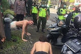 Two men doing push-ups on the streets of Bali surrounded by police officers.