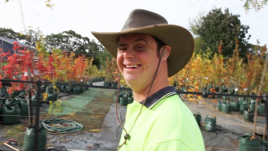 Man wearing hi-vis shirt and Akubra hat stands in garden centre with saplings in background