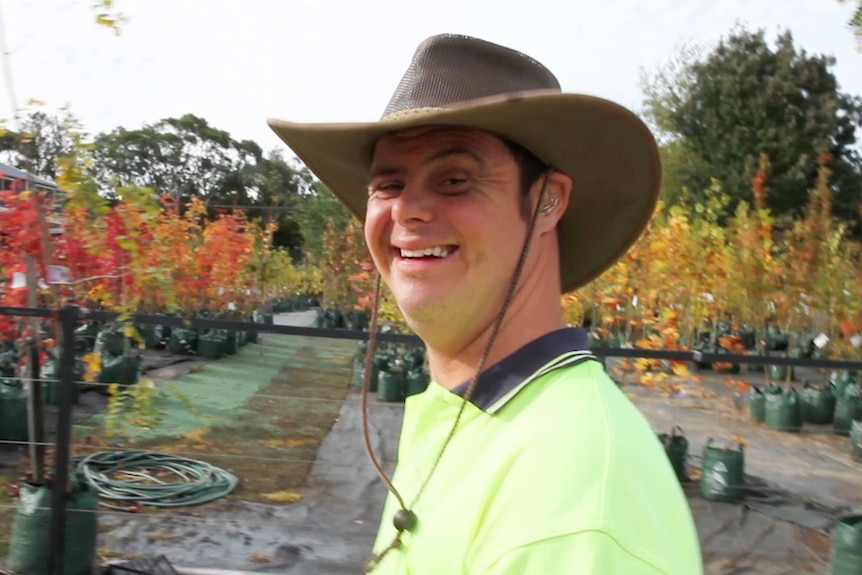 Man wearing hi-vis shirt and Akubra hat stands in garden centre with saplings in background