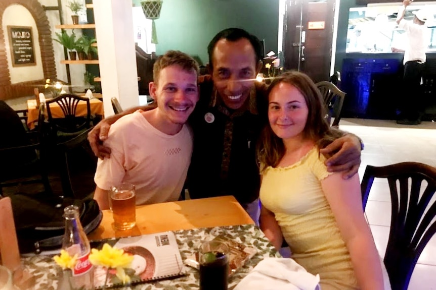 A Balinese man hugs a couple at a dinner table