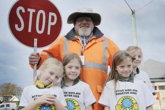 Brett smiles at the camera while holding a stop sign, as four children stand in front of him, smiling.