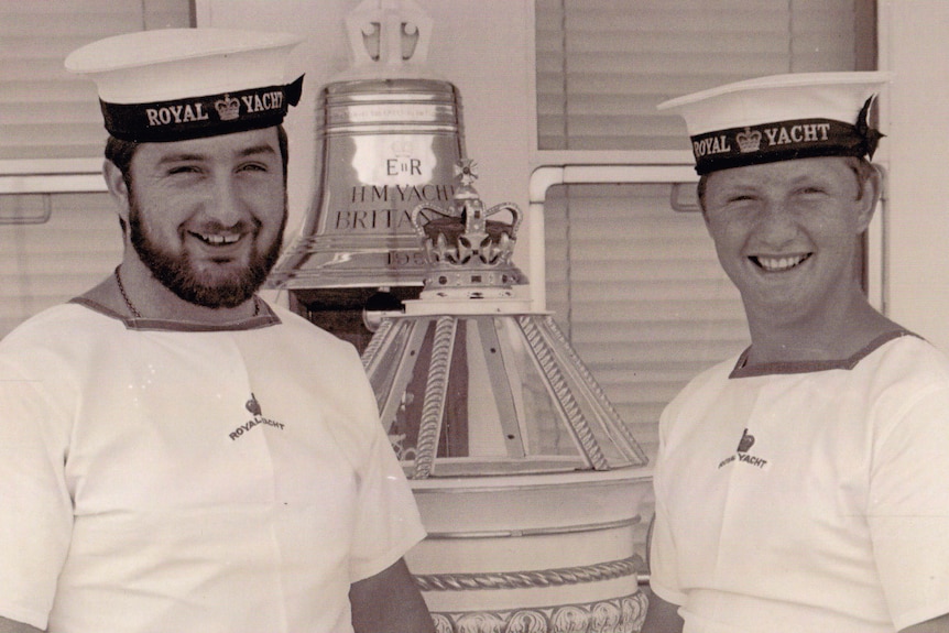 Two Navy officers stand on a yacht. 