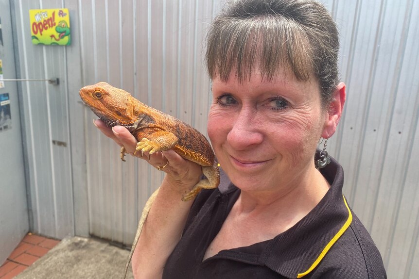 Woman holds bearded dragon near her face as she smiles at the camera.