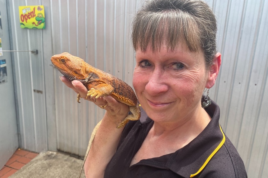 Woman holds bearded dragon near her face as she smiles at the camera.