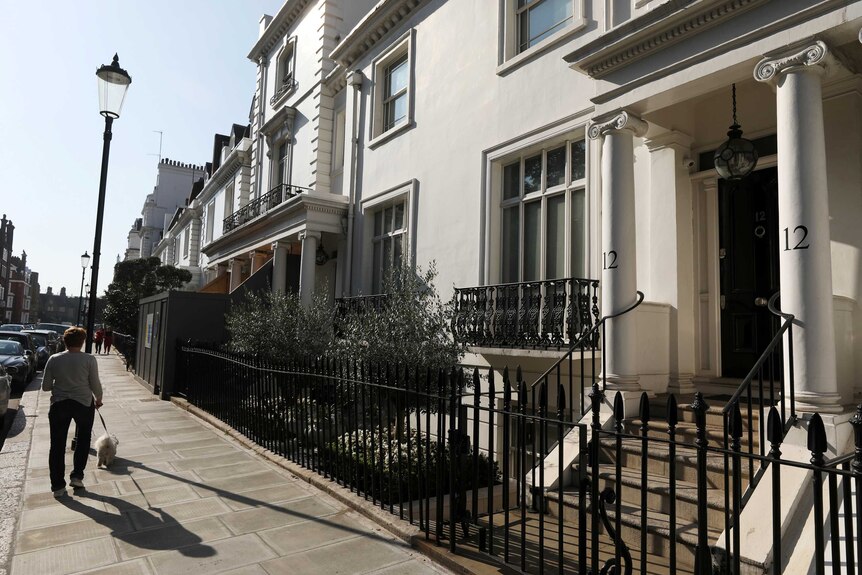 A woman walks along a street outside a white coloured house in London.