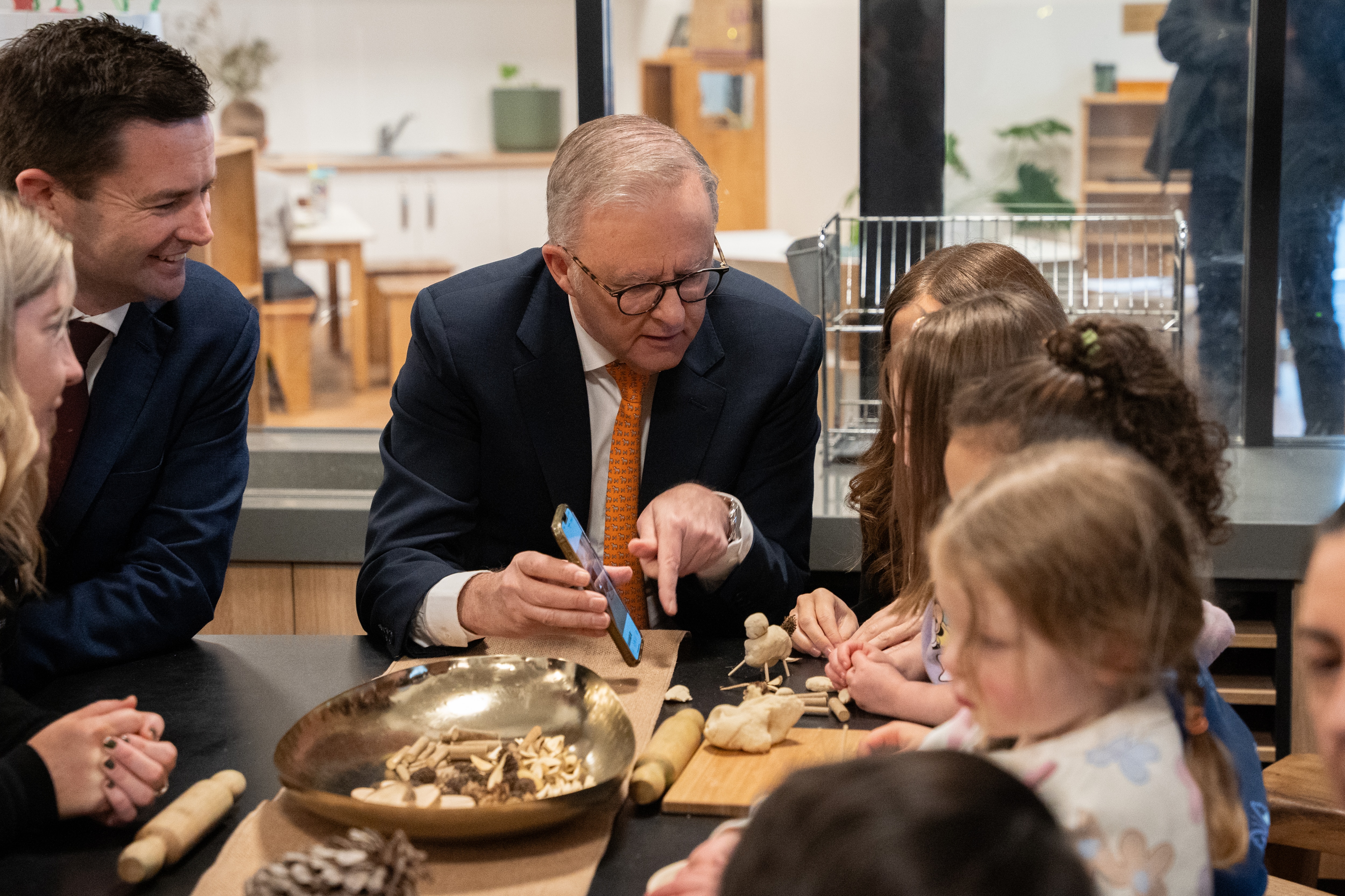 Anthony Albanese shows a child something on his phone.