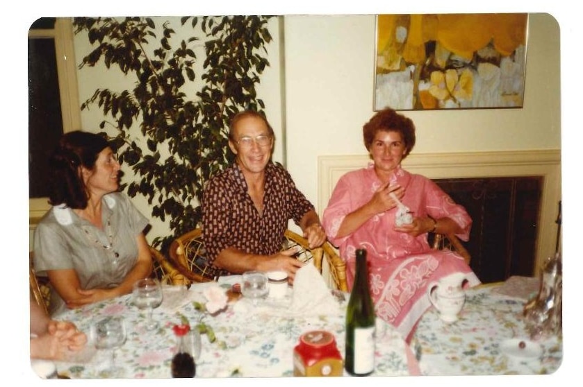 A photograph from the 80s showing a man and two women sitting on cane chairs in a living room, laughing.