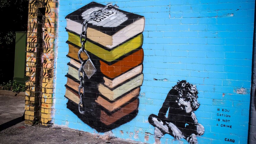A mural showing a child sitting on the ground beside a stack of books chained together.