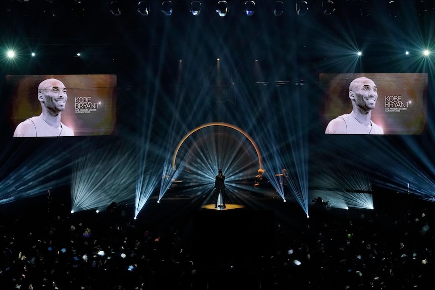 Kobe Bryant's face is on two large screens on either side of a darkened room. 