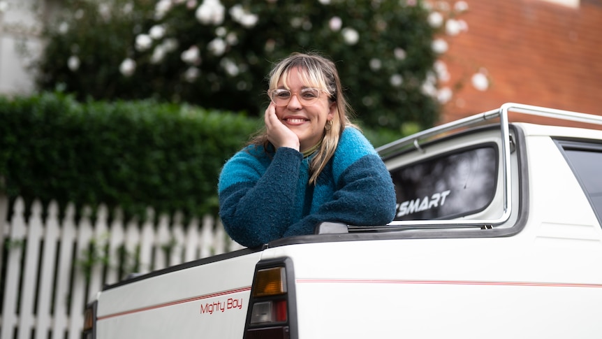 Portrait of a woman with her white, small, vintage car.
