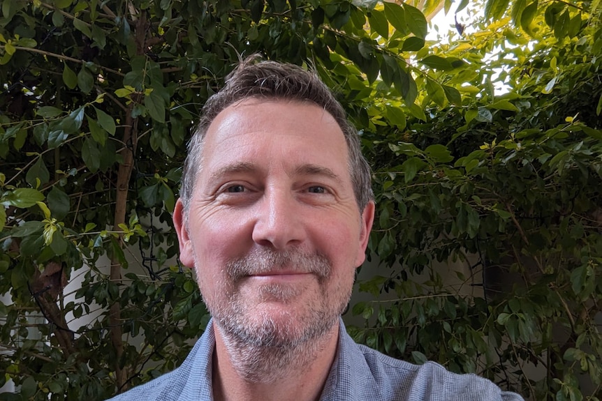 An image of William Price smiling in a grey shirt in front of greenery 