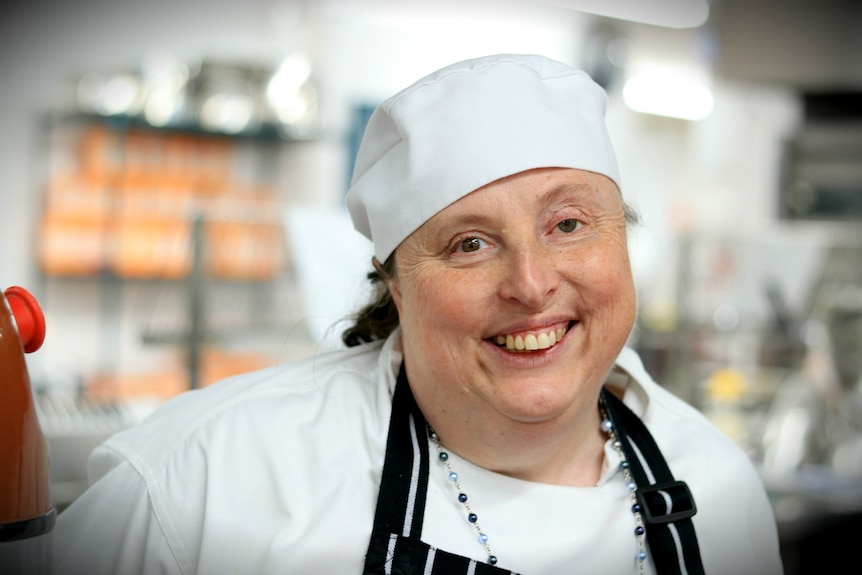 Sarah Elliot smiles at the camera wearing a chef hat and coat.