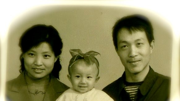 An old photo of a baby with a bow in her hair and her parents