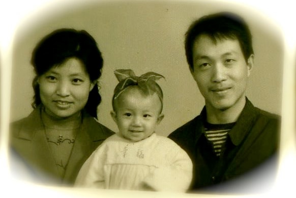 An old photo of a baby with a bow in her hair and her parents