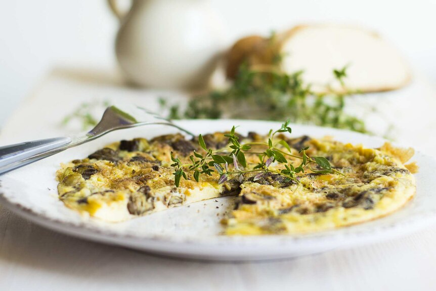 Close up of an omelette with fresh herbs on a white plate and table setting.